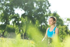 Young woman meditating peacefully in a park, surrounded by greenery. Morning Meditation Boosts people's Well-being. 